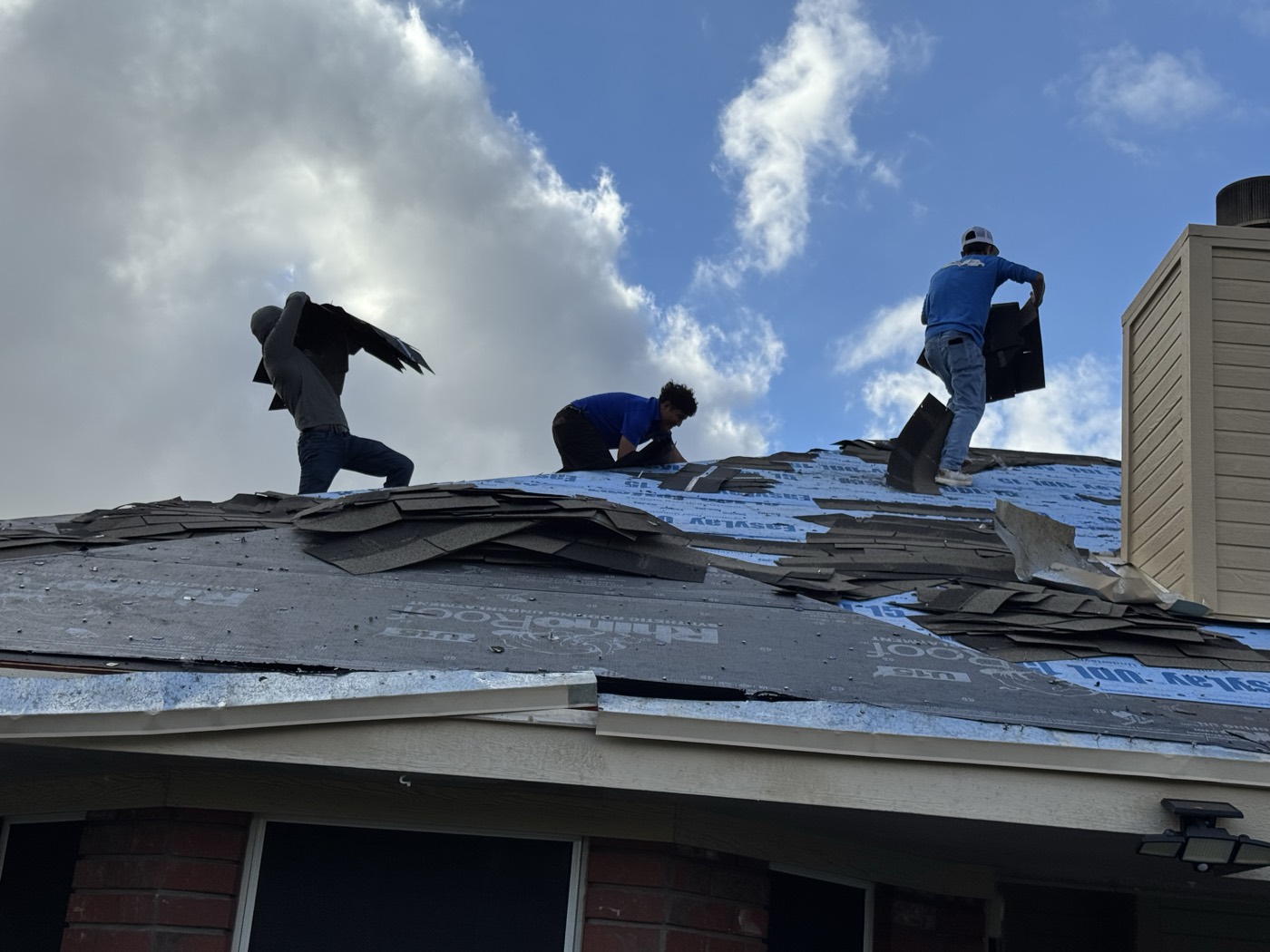 Crew carrying stacks of stripped shingles across blue RhinoRoof underlayment in Leander, TX