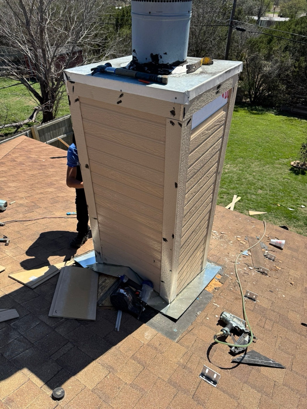 Chimney chase halfway through its rebuild with new siding going on and tools spread across the shingles in Leander, TX