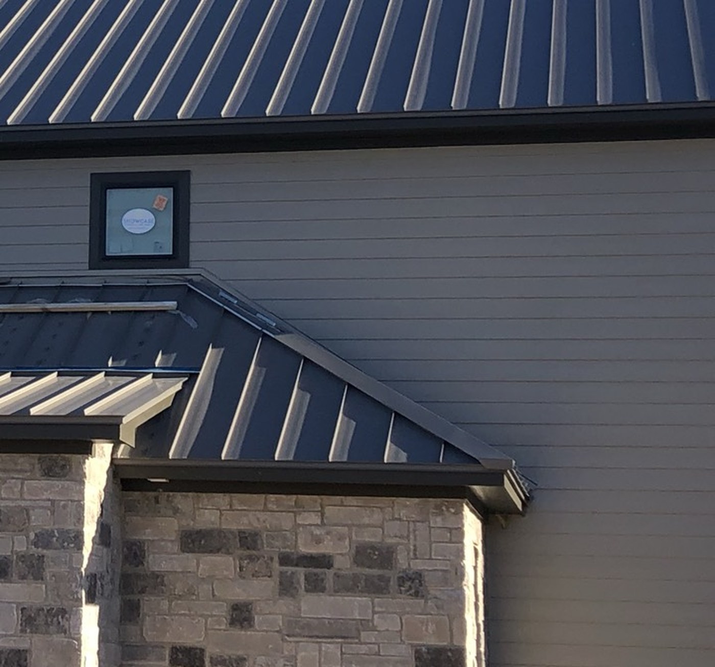 Dark seamless gutter and fascia running along the eave of a stone and siding building
