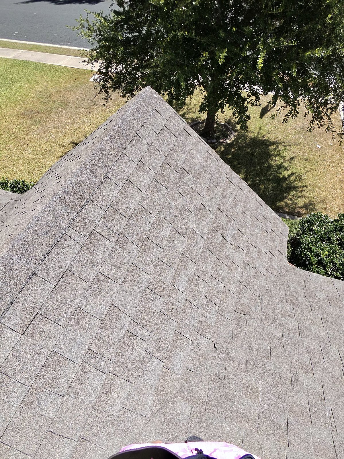 Looking down the ridge of a finished hip roof with the front lawn and street below in Leander, TX